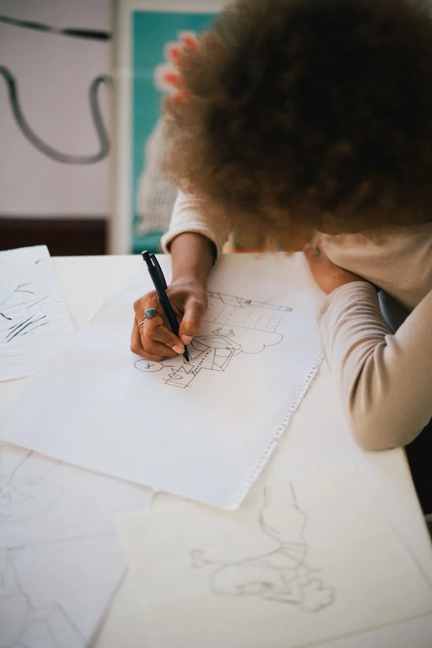 A student sketching game character concept art at a bright desk